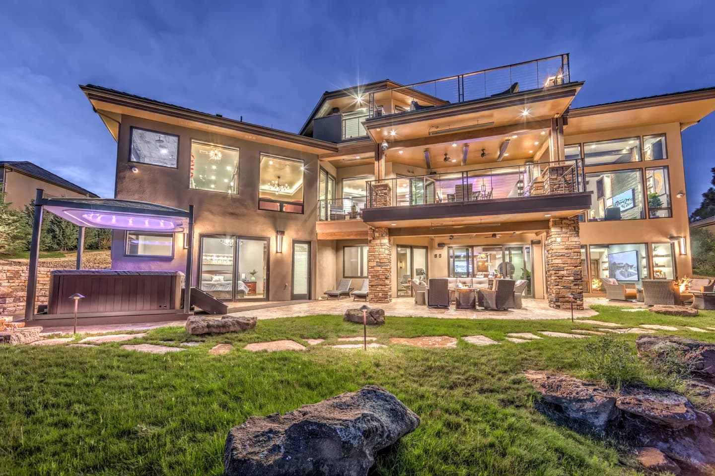 Rear elevation at dusk showing three levels of decks, walkout patio, spa and landscaped lawn